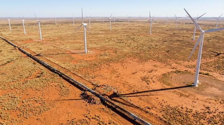 SPIE покупает Worley Power Services для экспансии на энергорынке Австралии Ветряная электростанция с рядами турбин и магистральный газопровод в засушливом красноземном пейзаже Австралии под ярким солнцем.